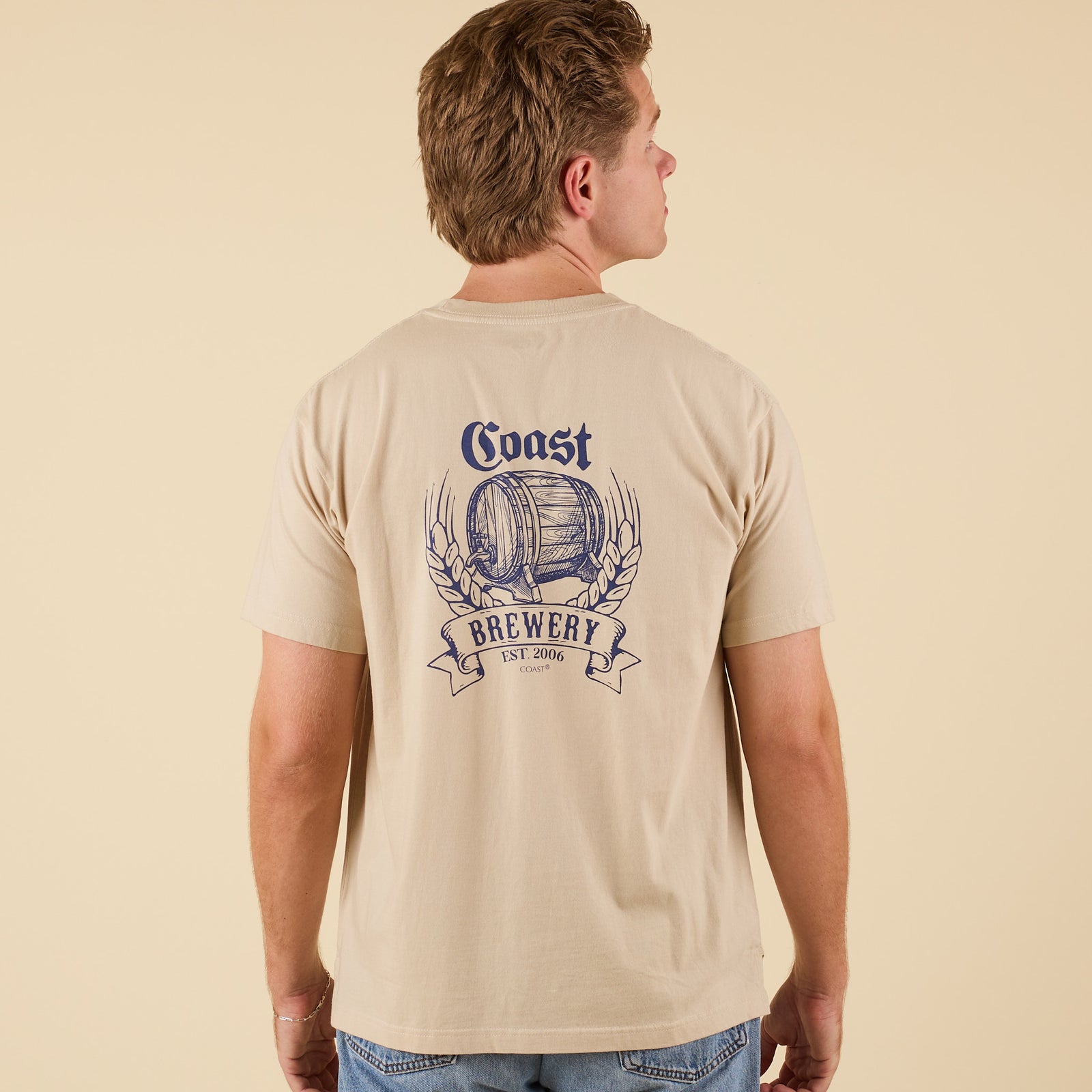 Back view of COAST Beer Barrel short sleeve pocket tee in sand with large brewery barrel graphic and wheat design.