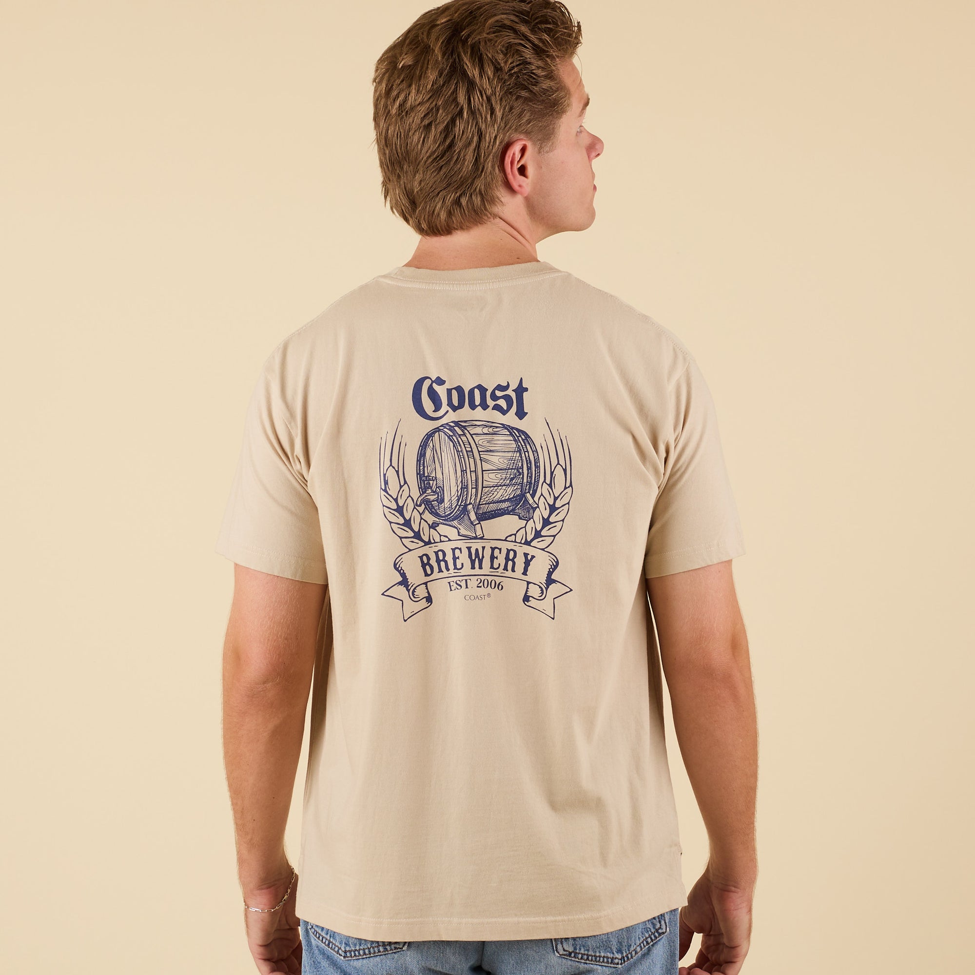 Back view of COAST Beer Barrel short sleeve pocket tee in sand with large brewery barrel graphic and wheat design.