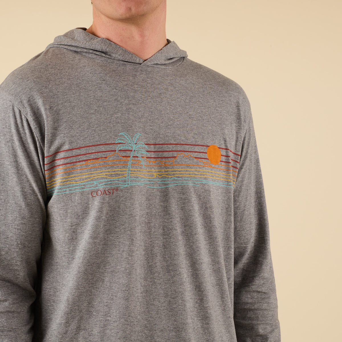 Close-up of COAST Palm Sunset graphic with colorful retro stripes, palm tree, and orange sun on grey performance hoodie.