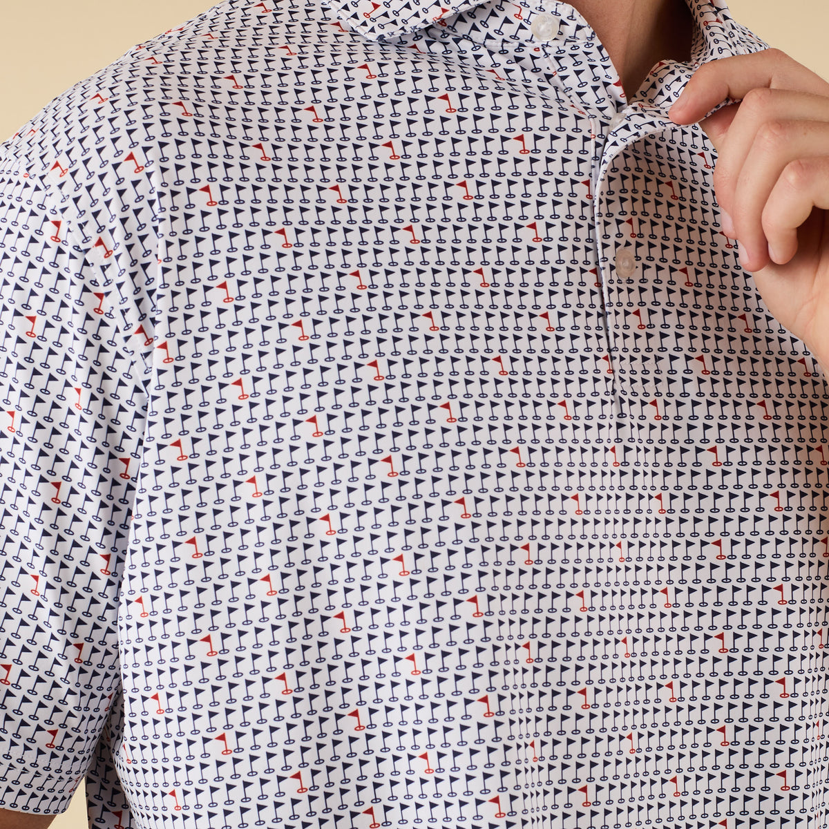Close-up of white polo shirt fabric with navy and red golf flag print, showing partial collar and buttons as man adjusts collar.