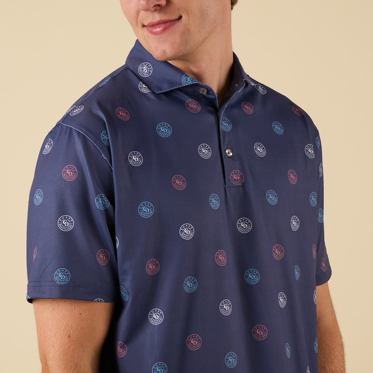 Close-up of man wearing a navy short-sleeve polo shirt with all-over red, white, and blue Coast circular logo print.