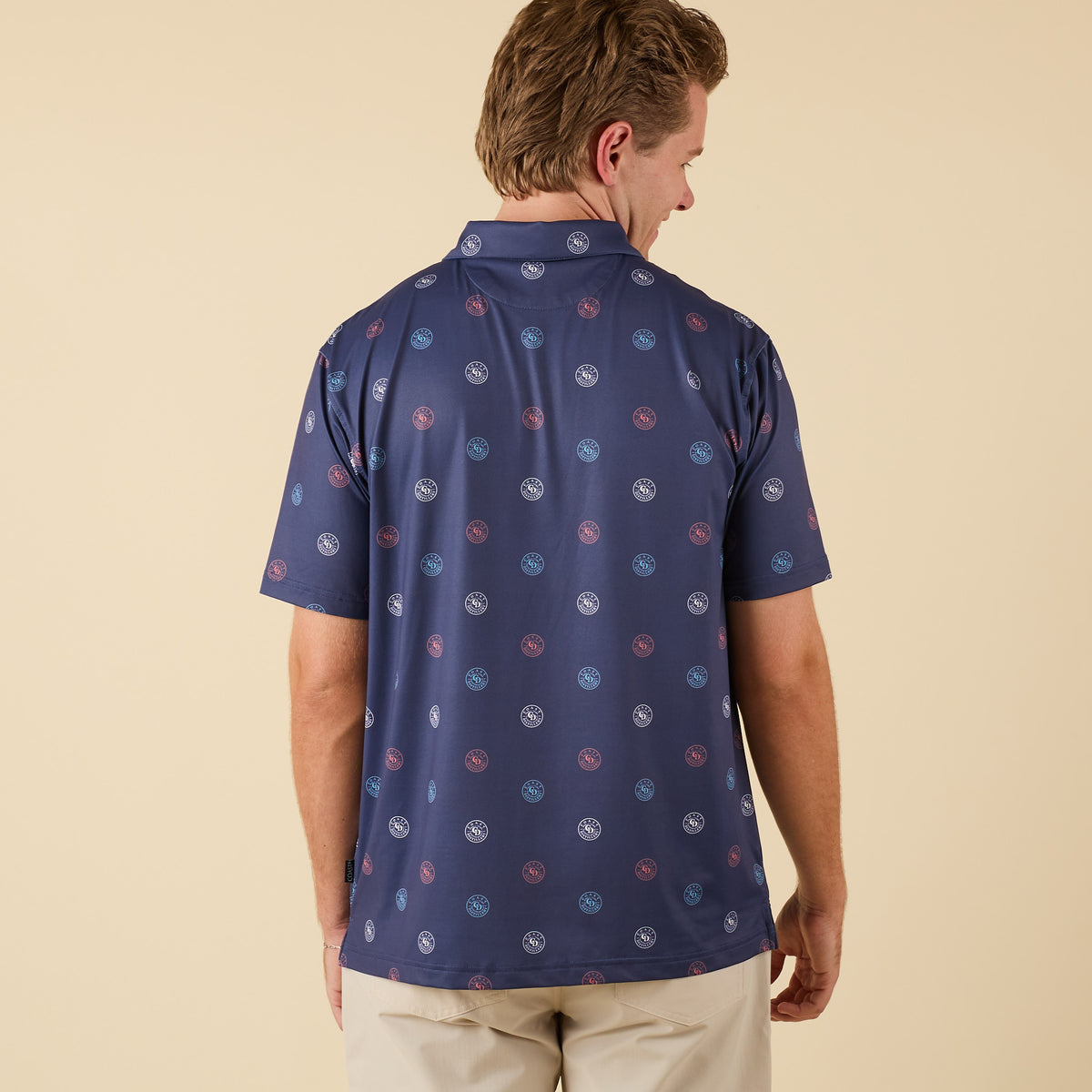 Man wearing a navy printed short-sleeve polo shirt with Coast circular logo pattern, shown from the back with hands by his side.
