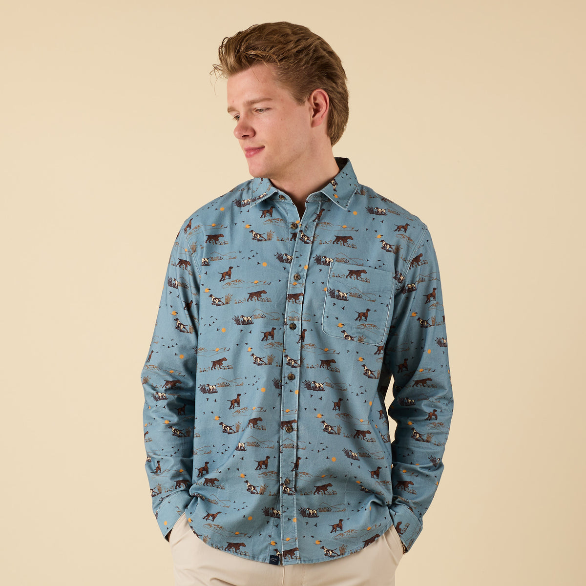 Man wearing blue long sleeve button-down shirt with hunting dog scene print, front view.
