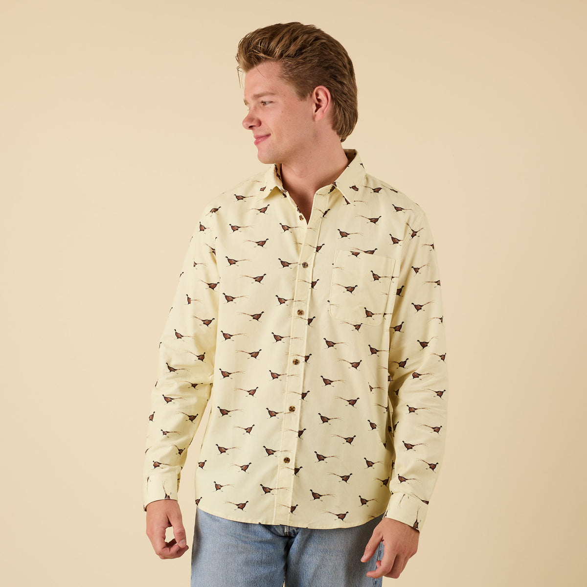 Man smiling in yellow pheasant print button-down shirt, angled view.