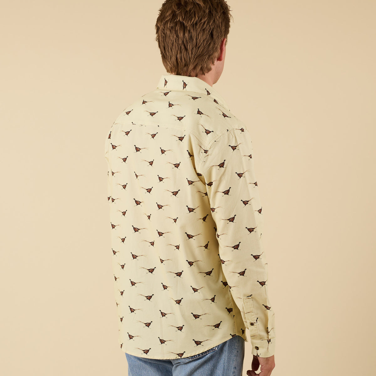Back view of man wearing yellow pheasant print long sleeve shirt.