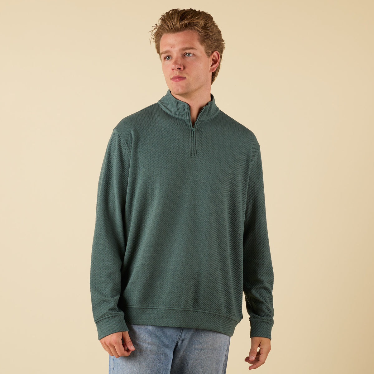 Man wearing a dark green textured quarter zip pullover with a stand collar and relaxed fit.