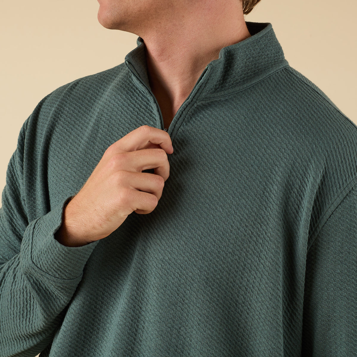 Man wearing a dark green textured quarter zip pullover with a stand collar and relaxed fit.