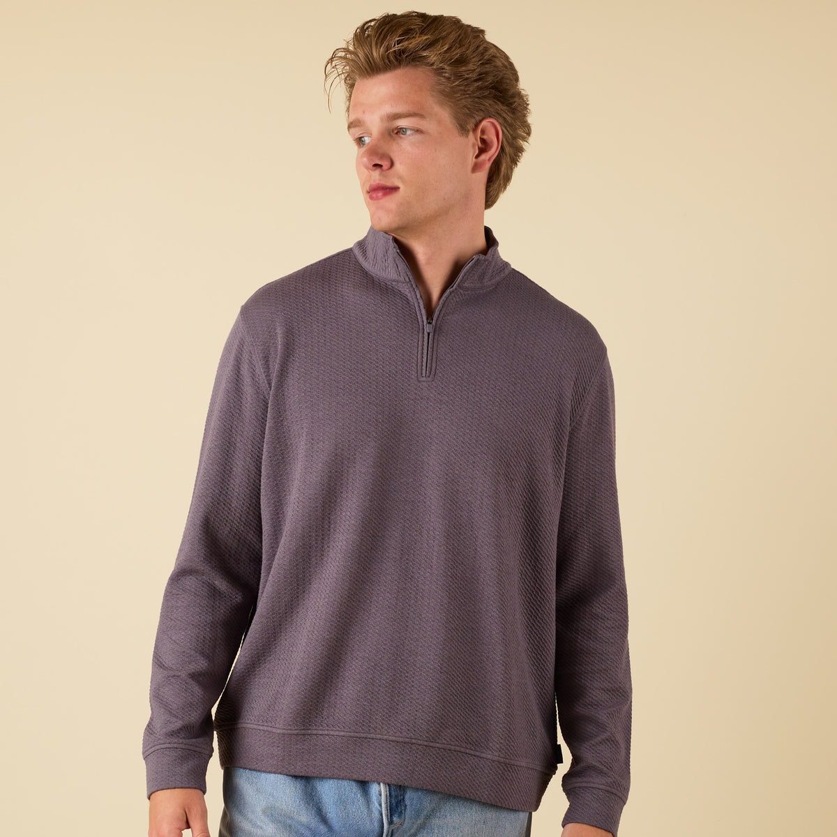 Man wearing a dark grey textured quarter zip pullover with a stand collar and relaxed fit.