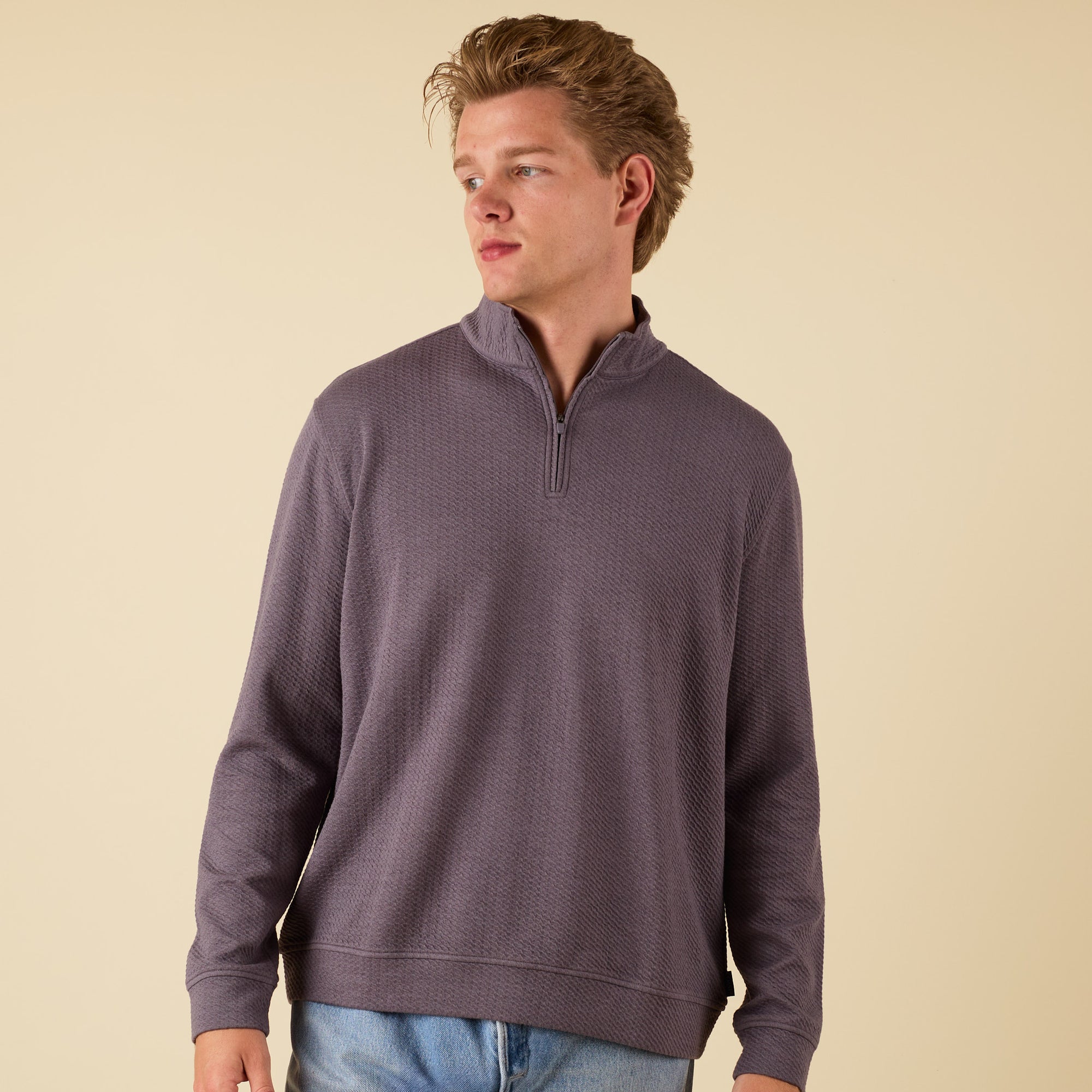 Man wearing a dark grey textured quarter zip pullover with a stand collar and relaxed fit.