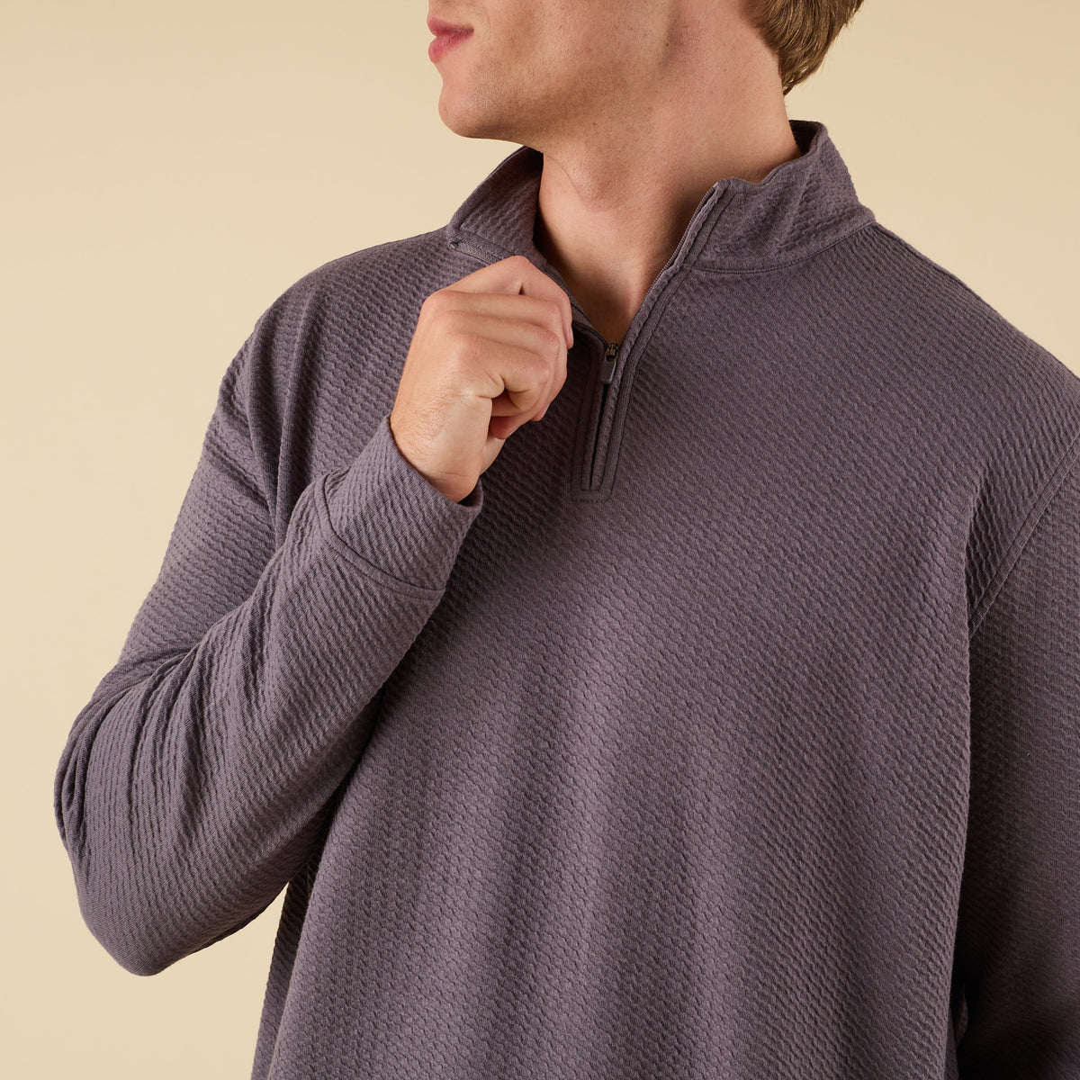 Man wearing a dark grey textured quarter zip pullover with a stand collar and relaxed fit.