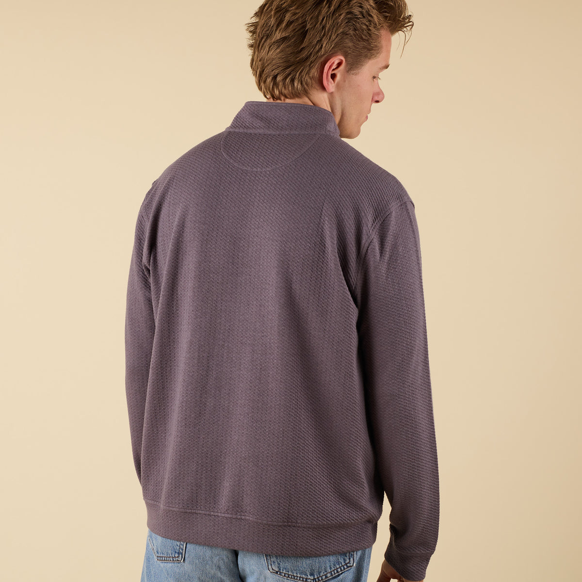Man wearing a dark grey textured quarter zip pullover with a stand collar and relaxed fit.