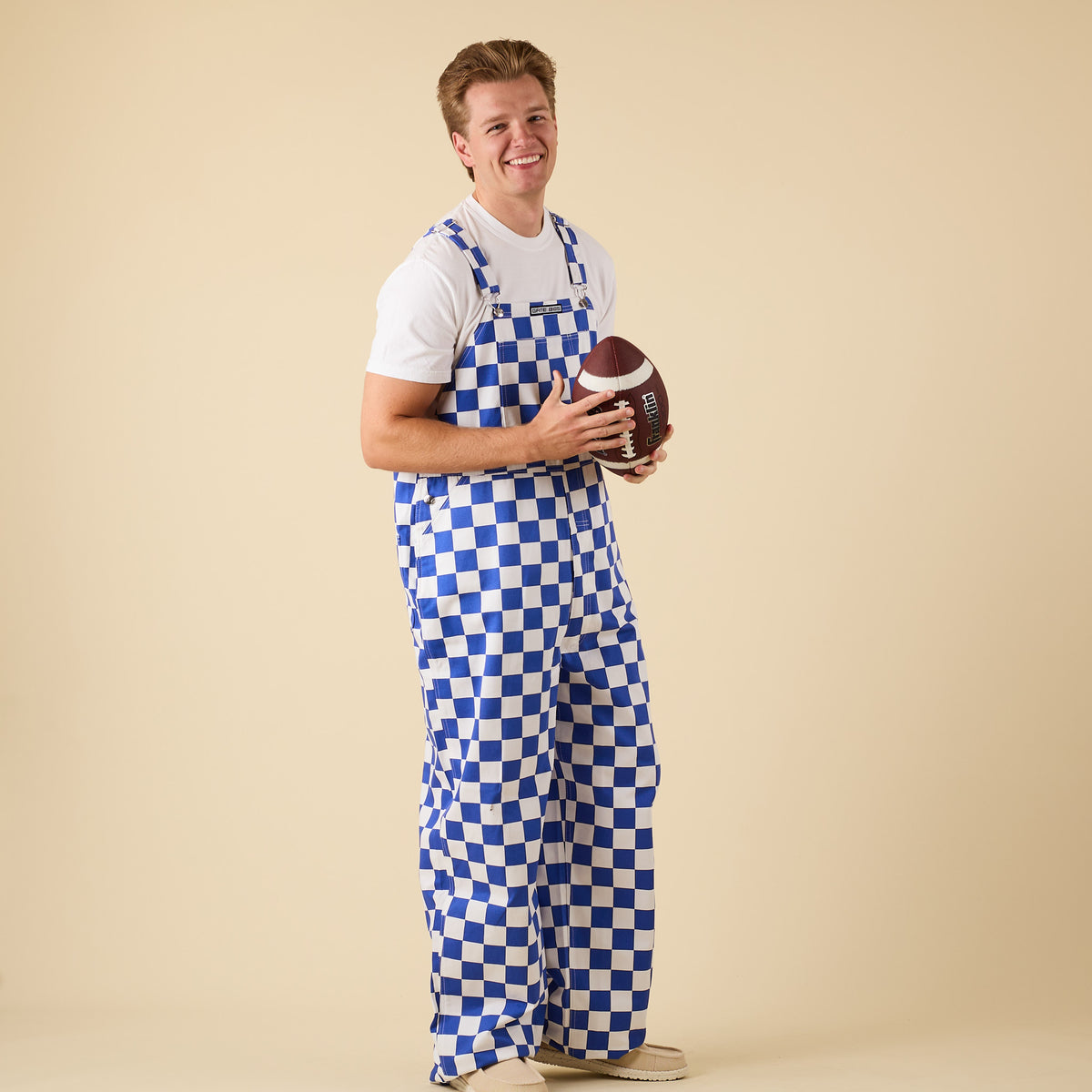 Man posing for a product photo wearing blue and white checkered overalls.