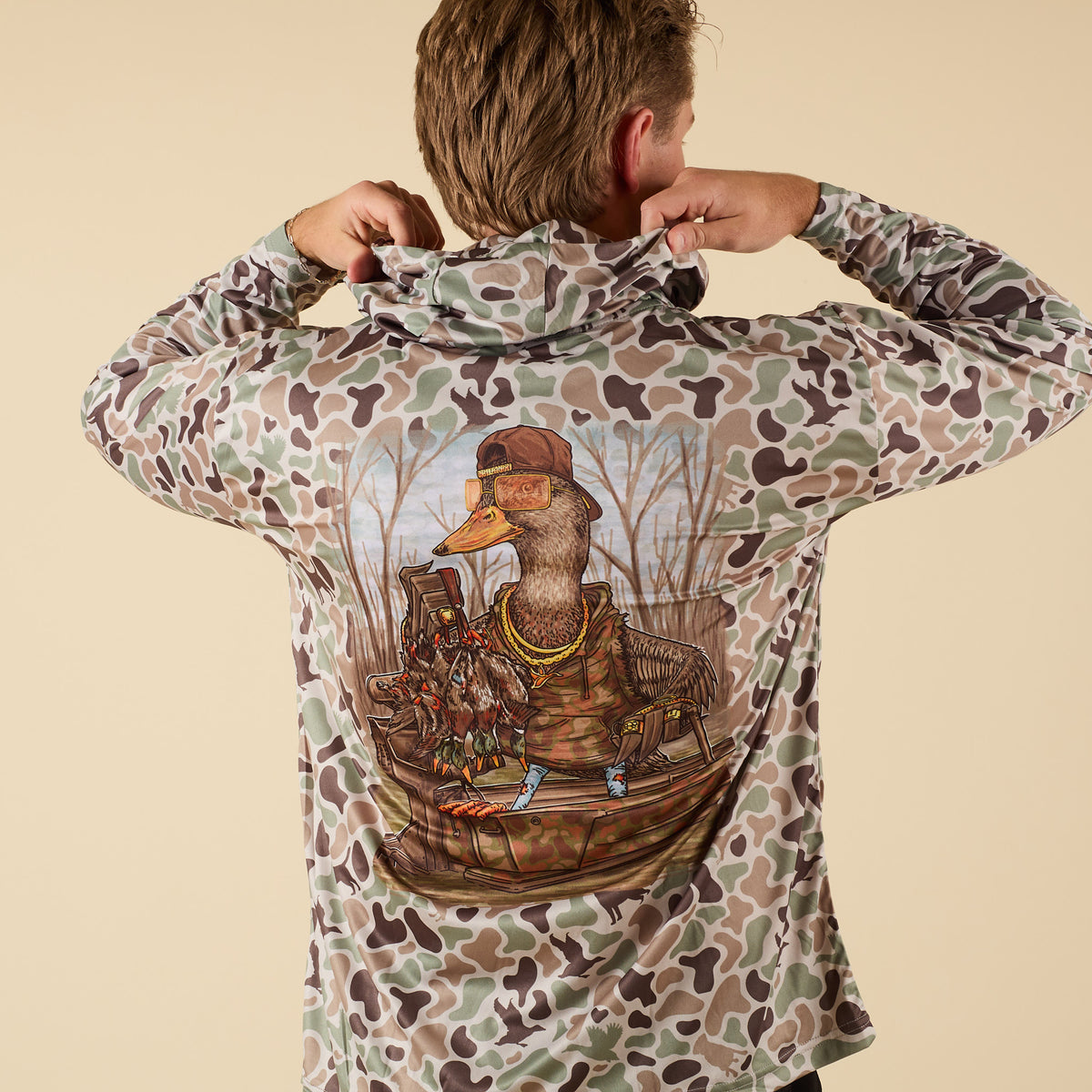 Person wearing a camouflage performance shirt with a graphic of a duck in a boat on the back.