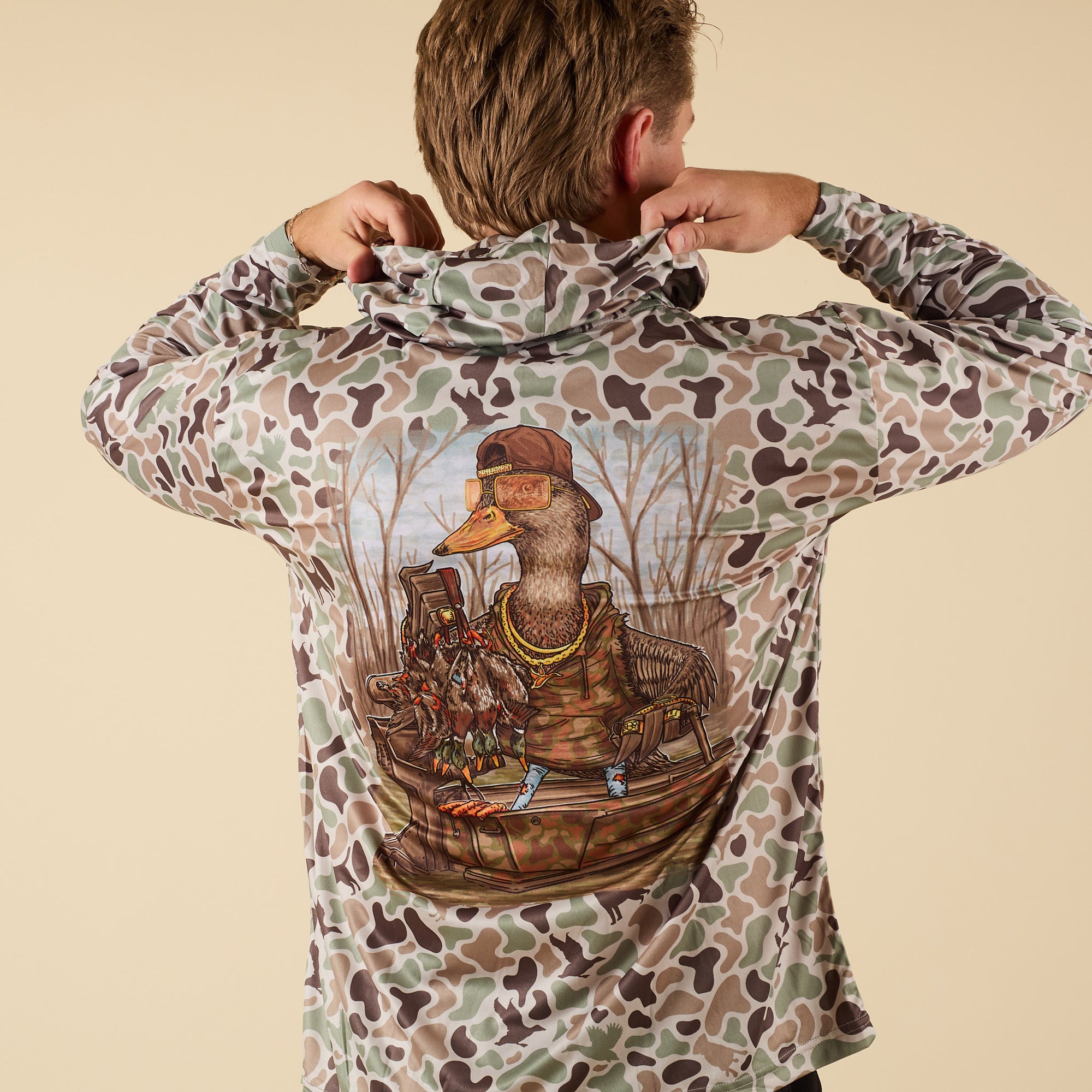 Person wearing a camouflage performance shirt with a graphic of a duck in a boat on the back.