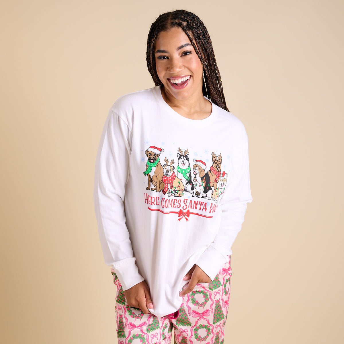 Woman wearing a white long-sleeve shirt with a graphic design of dogs in Santa hats on a beige background