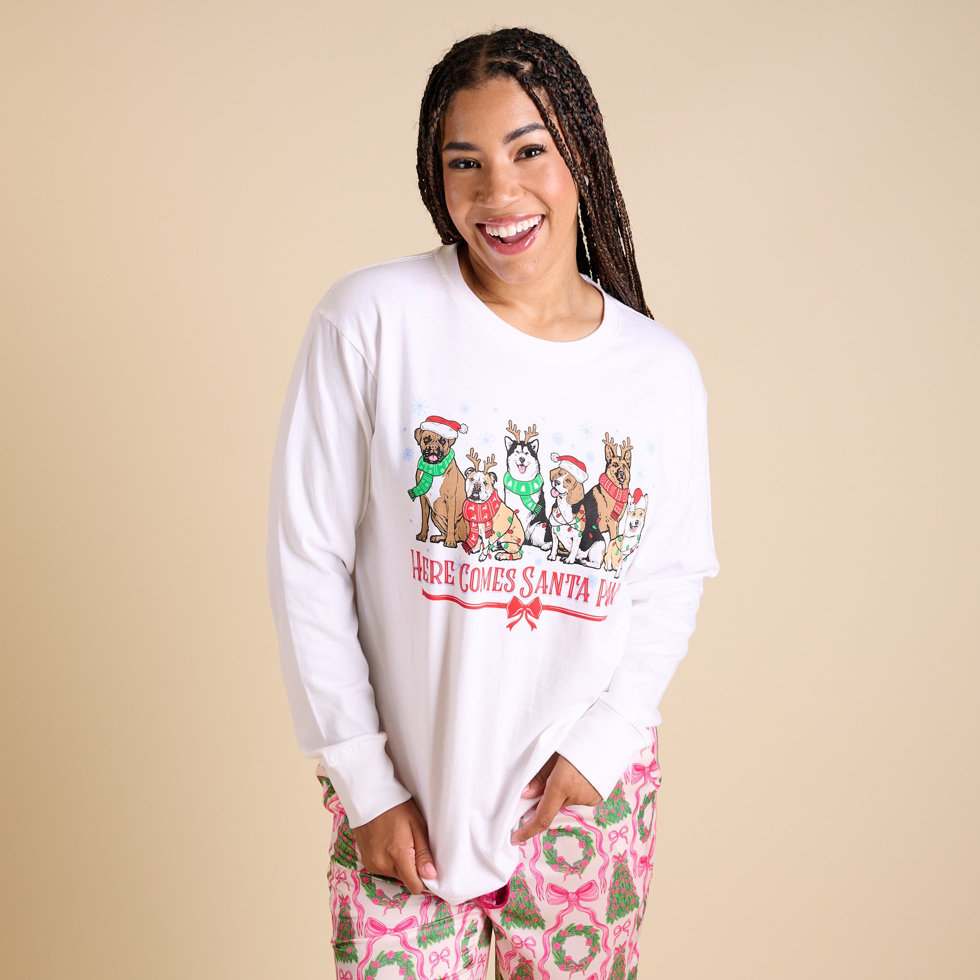Woman wearing a white long-sleeve shirt with a graphic design of dogs in Santa hats on a beige background