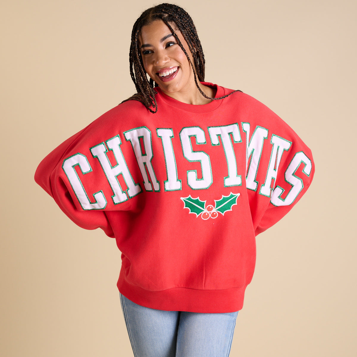 Person wearing a red 'Christmas' sweater with holly design on a beige background