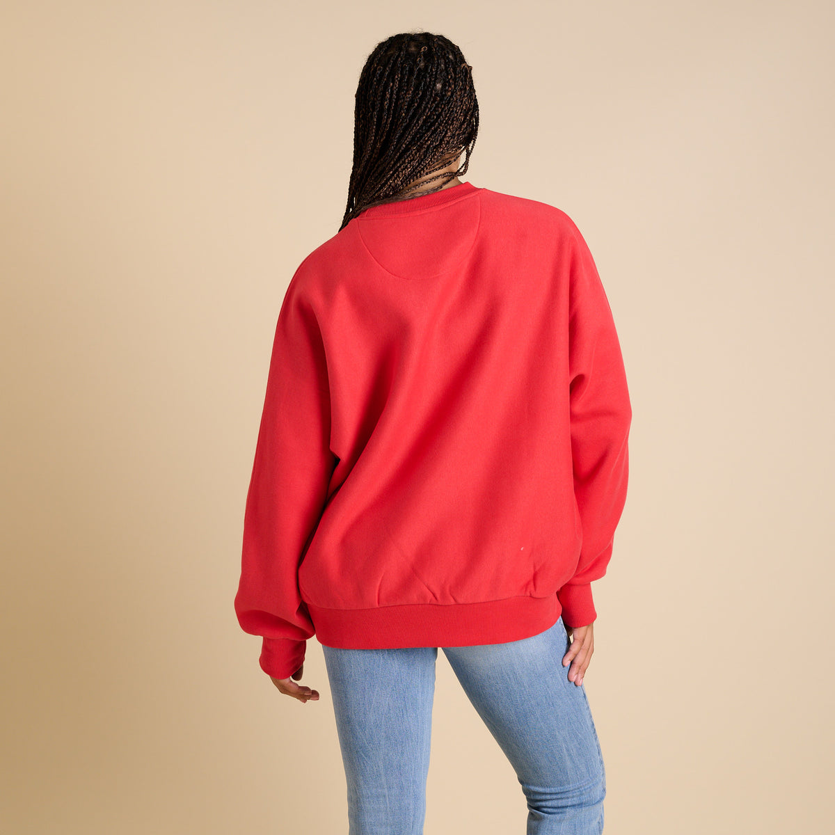 Person wearing a red sweatshirt and blue jeans on a beige background