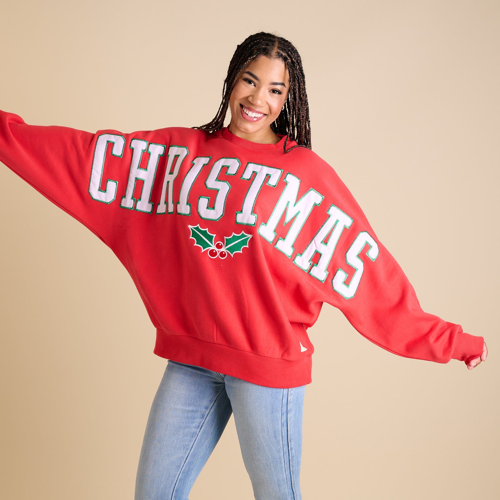 Person wearing a red 'CHRISTMAS' sweatshirt with holly design on a beige background