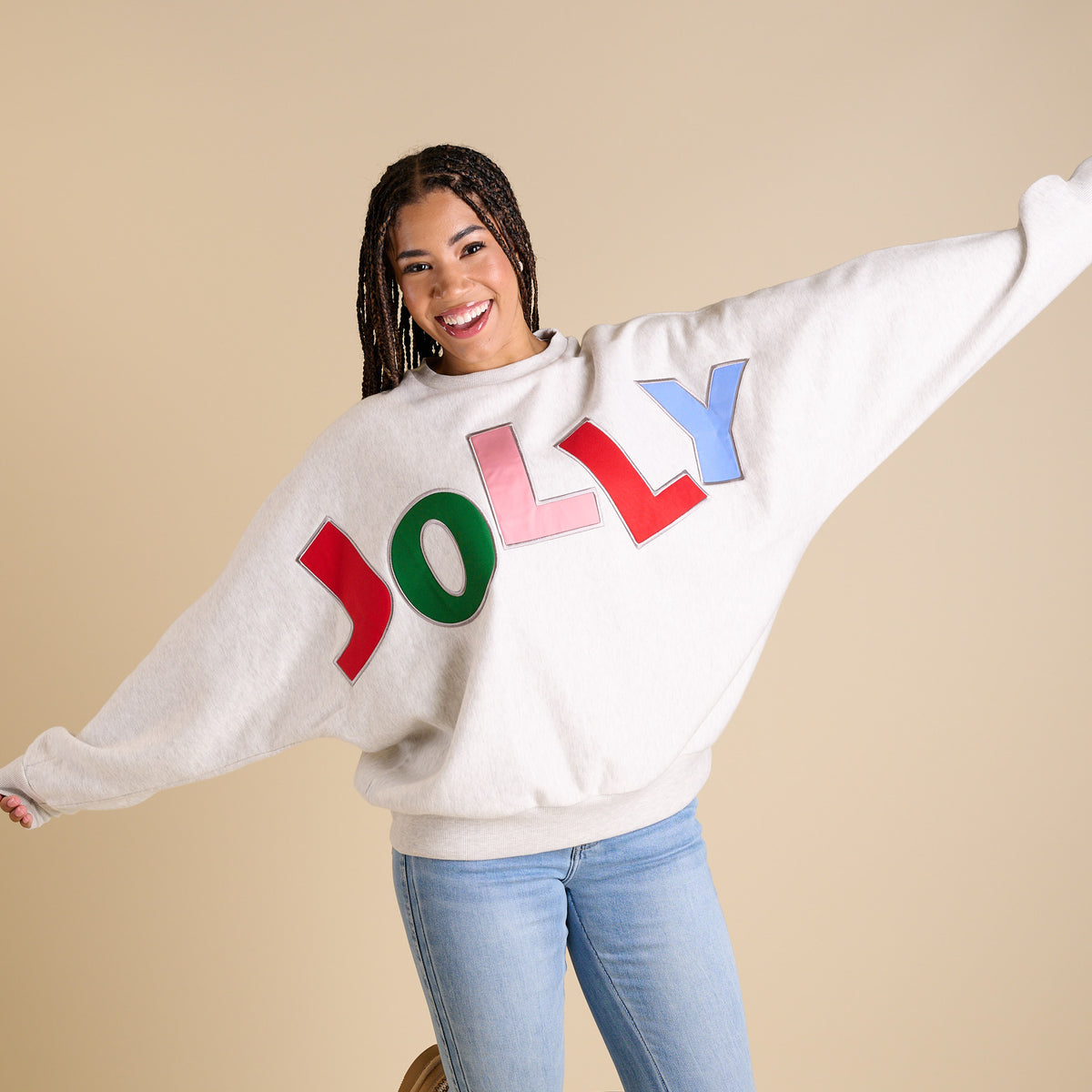 Person wearing a white sweater with colorful letters spelling 'JOLLY' against a beige background