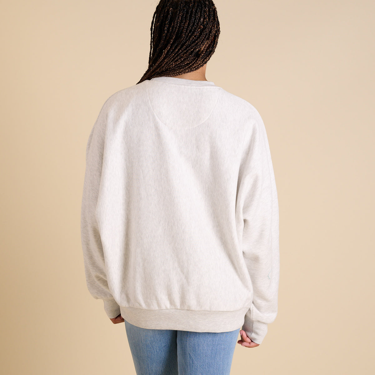 Person wearing a light gray sweatshirt and blue jeans on a beige background