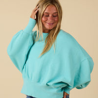 Woman posing for a photo in a teal blue oversized sweatshirt.