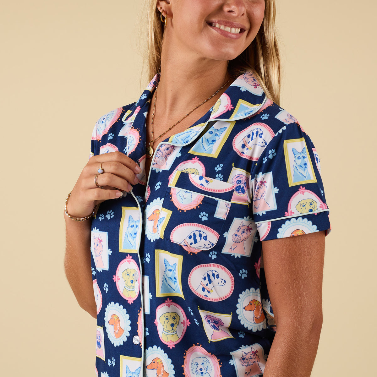 Woman wearing blue pajama top with colorful dog portrait print, short sleeves, and button front detail.