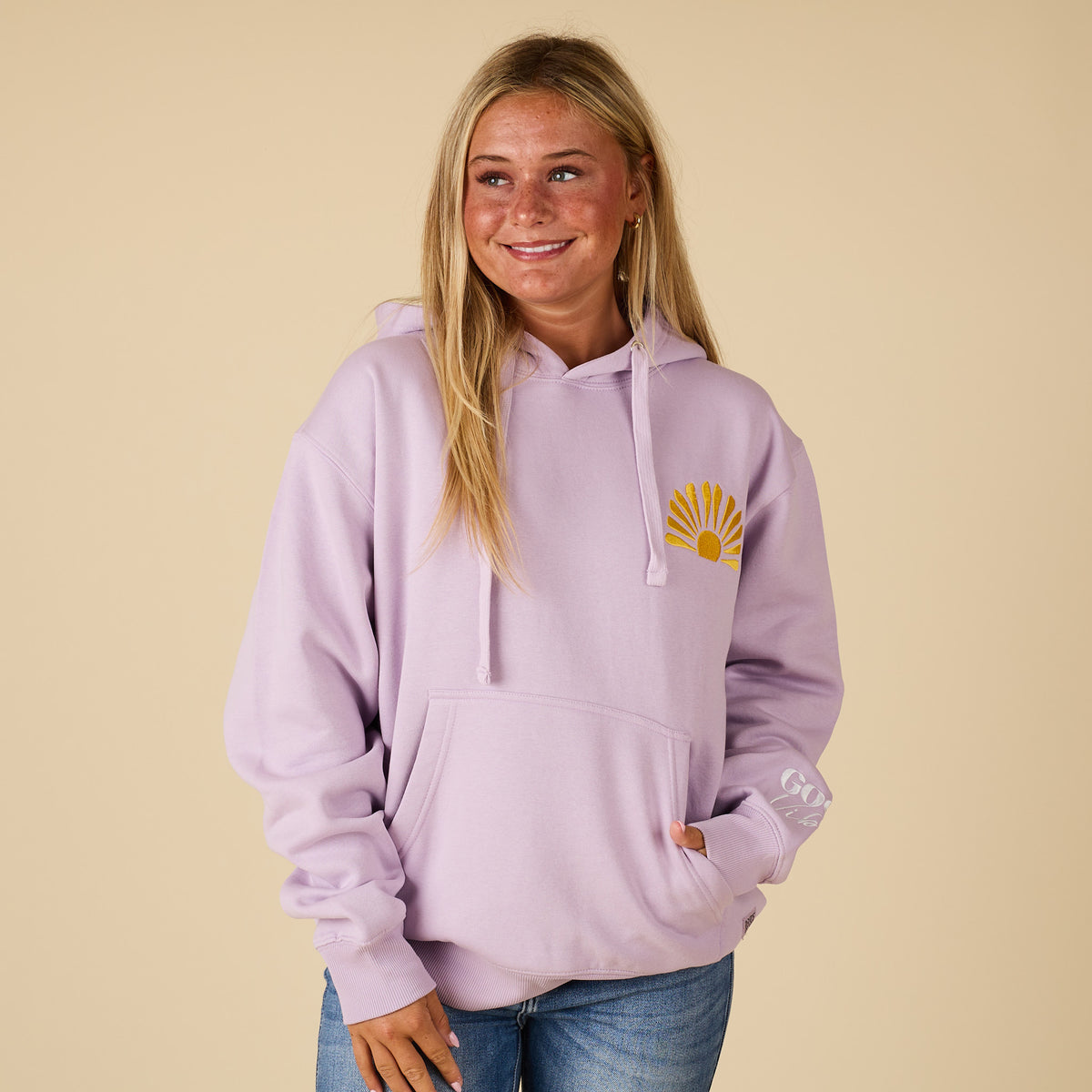 Person wearing a light purple hoodie with a yellow logo on a beige background