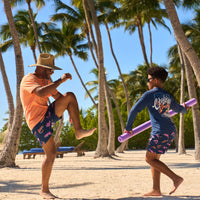 A father and son playing on the beach with a pool noodle.