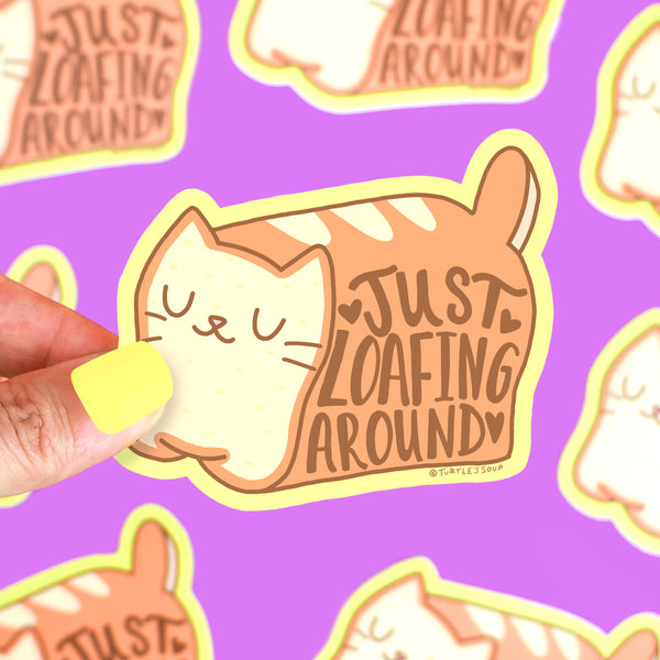Sticker of a cat with 'Just Loafing Around' text held by a hand on a purple background with similar stickers.
