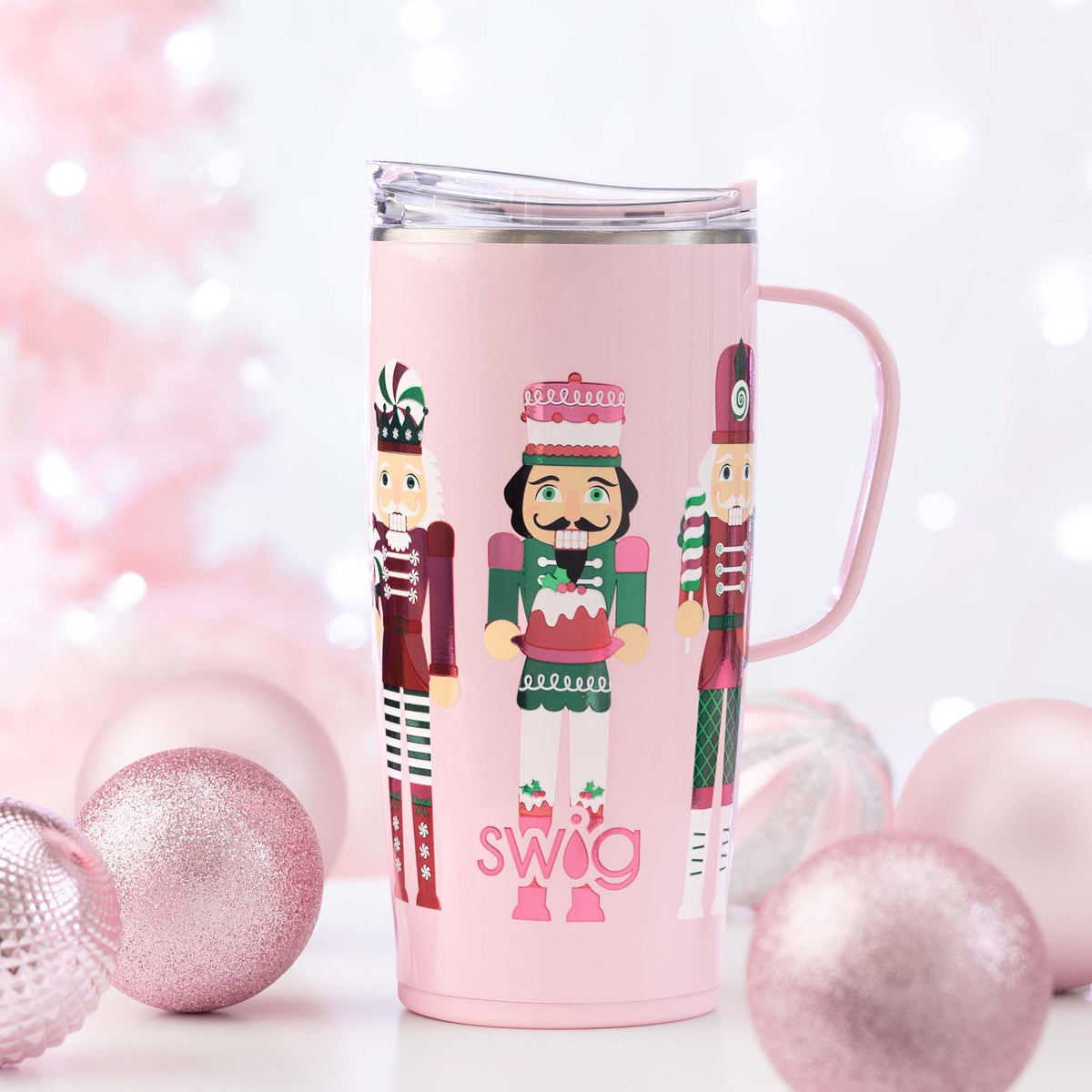 Pink mug with nutcracker design and 'SWIG' text, surrounded by pink ornaments on a light background