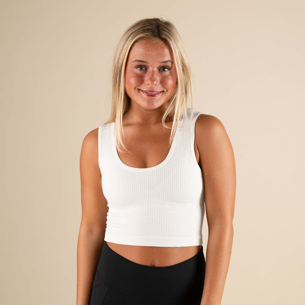 Woman wearing a white tank top against a beige background