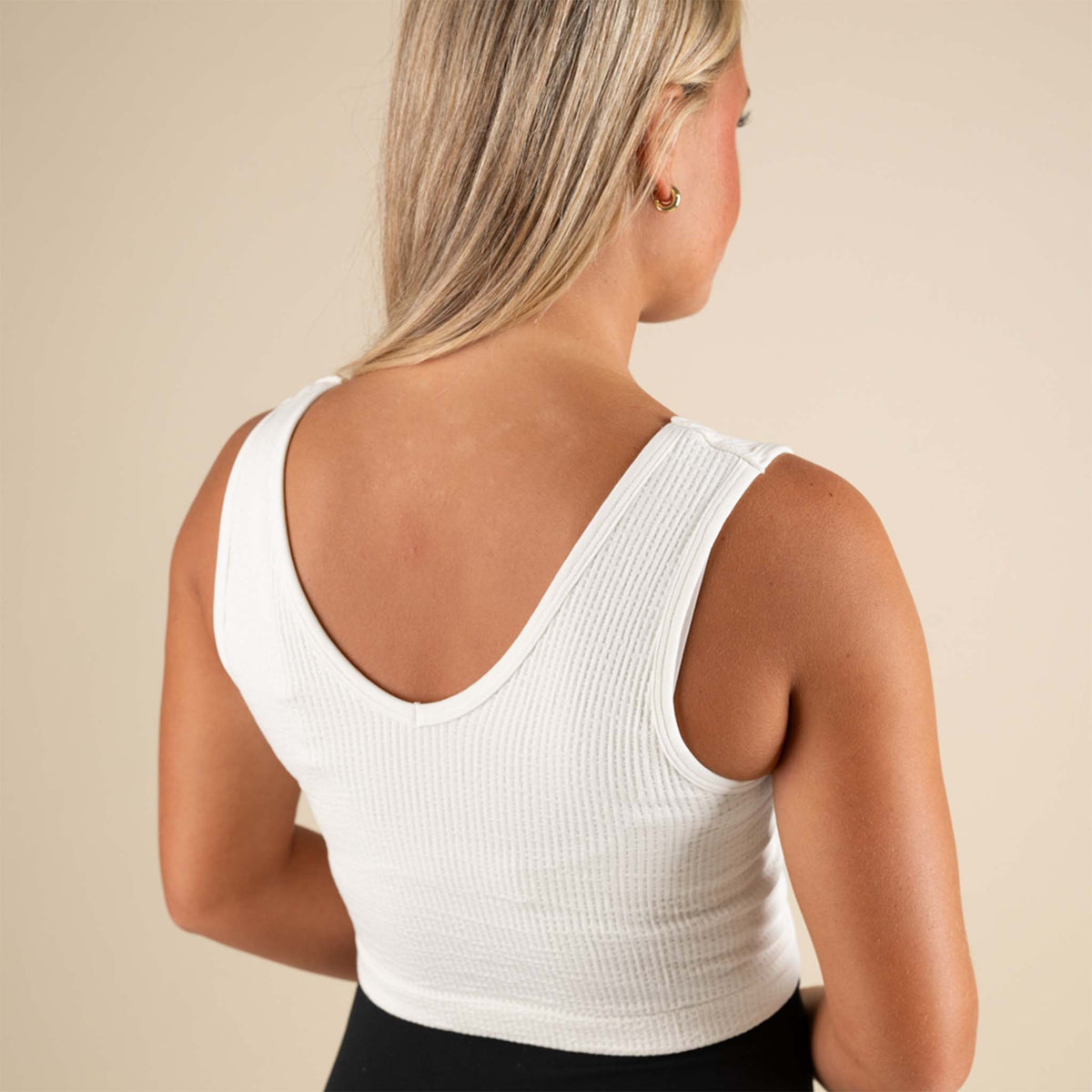 Woman wearing a white sleeveless top against a beige background