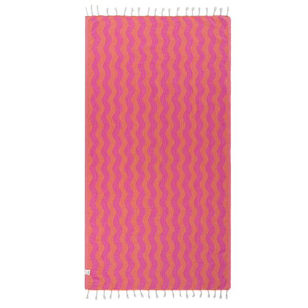 Pink and orange wavy patterned Sand Cloud towel with white tassels on a white background