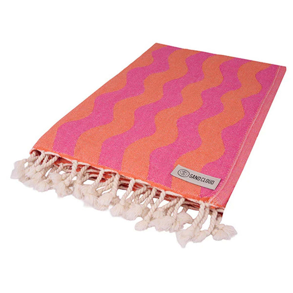 Pink and orange wavy patterned Sand Cloud towel with white tassels on a white background