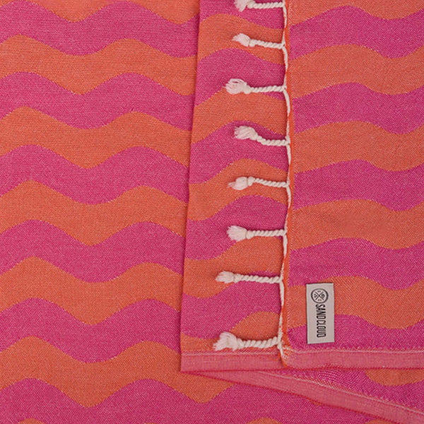 Pink and orange striped towel with tassels and a Sand Cloud label.