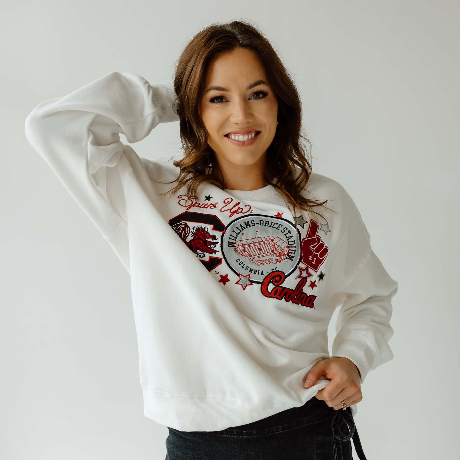Woman wearing white University of South Carolina crewneck sweatshirt with Williams-Brice Stadium, Gamecock logo, and “Spurs Up” graphic.