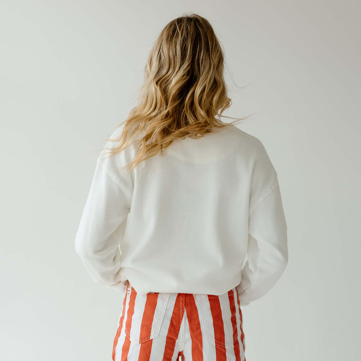 Woman wearing plain white cropped crewneck sweatshirt with no design, paired with red and white striped shorts.