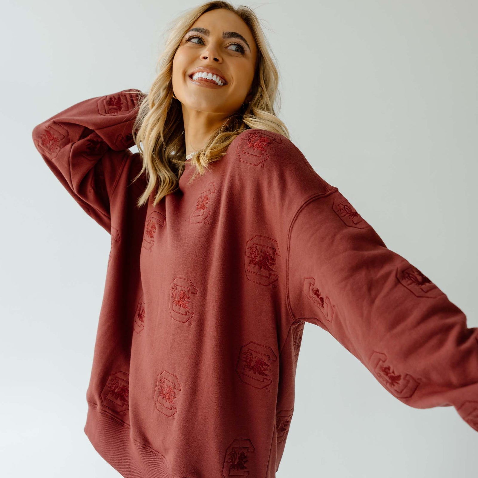 Woman wearing maroon crewneck sweatshirt with all-over embossed University of South Carolina Gamecock logos.