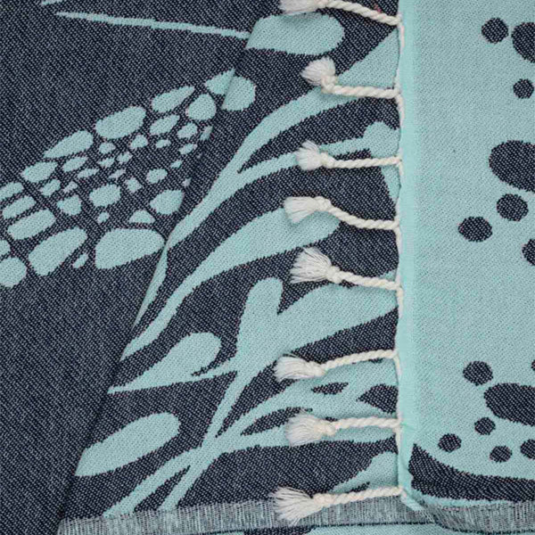 Close-up of a patterned fabric with navy blue and aqua green design and white tassles