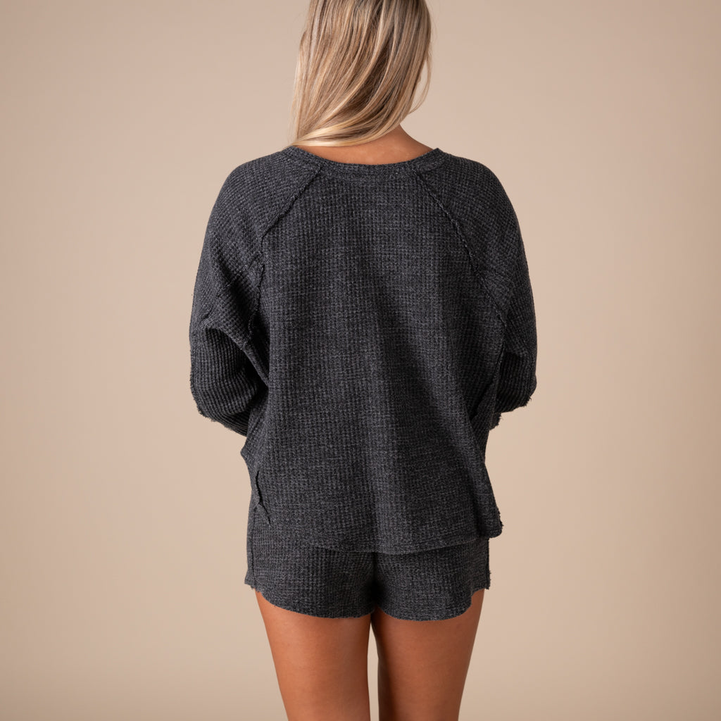 Person wearing a dark gray textured top and shorts on a beige background