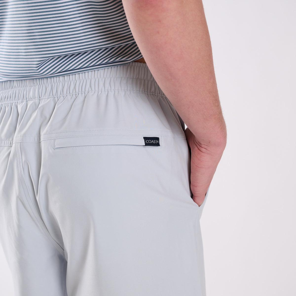 Man wearing light gray shorts and a striped shirt on a white background.