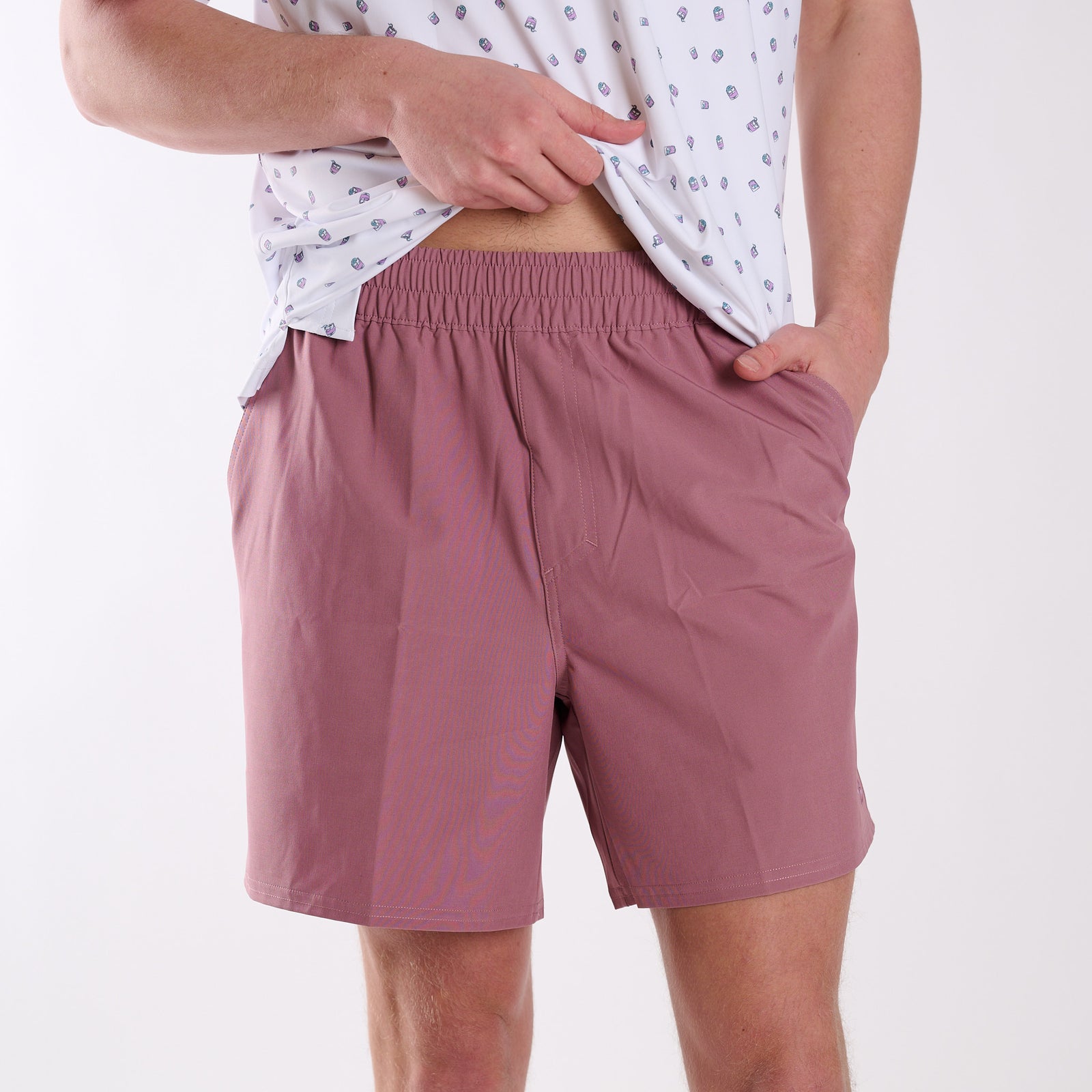 Man wearing dusty pink shorts and a white patterned shirt on a white background
