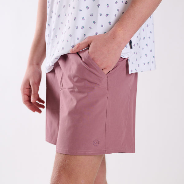 Man wearing dusty pink shorts and a white patterned shirt on a white background
