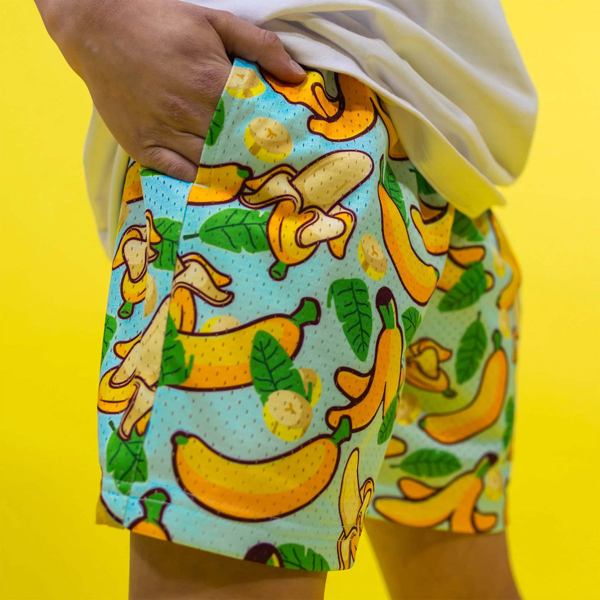 side image of boy wearing of Baseball Lifestyle 101 Youth Shorts tropical banana pattern with his hand in pocket.