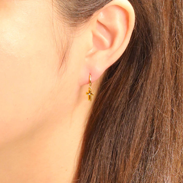 Do Everything In Love Gold Cross Huggie Earrings, Close-up of a woman wearing small gold hoop earrings with dangling polished cross charms.