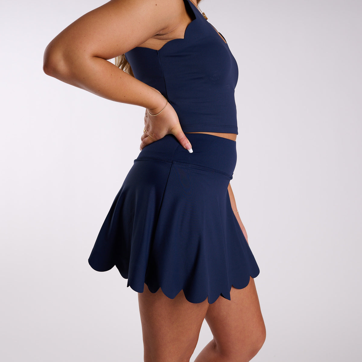 Woman wearing a Scallop Hem Active Skort in Navy in front of a white background.