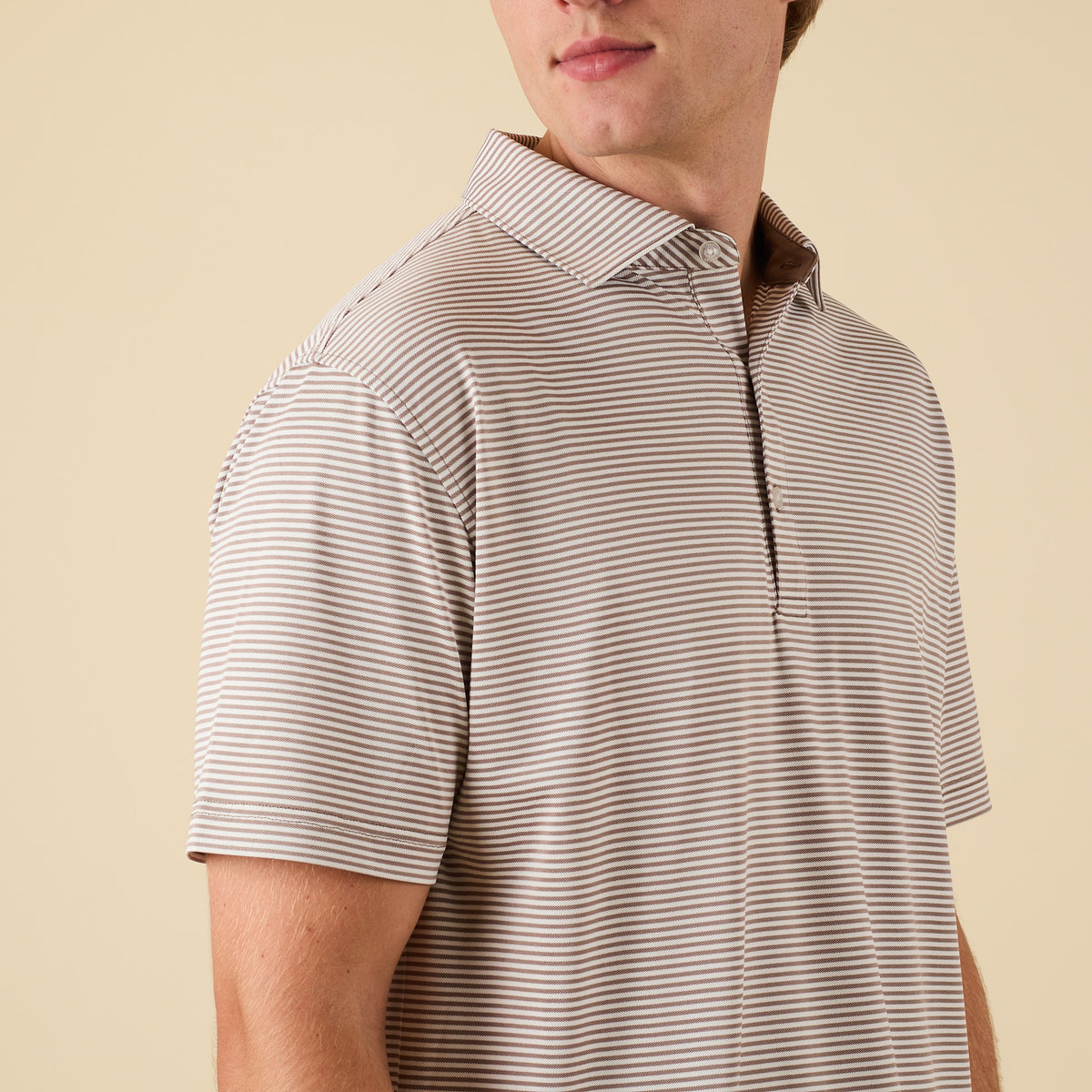 Man wearing a striped polo shirt against a beige background