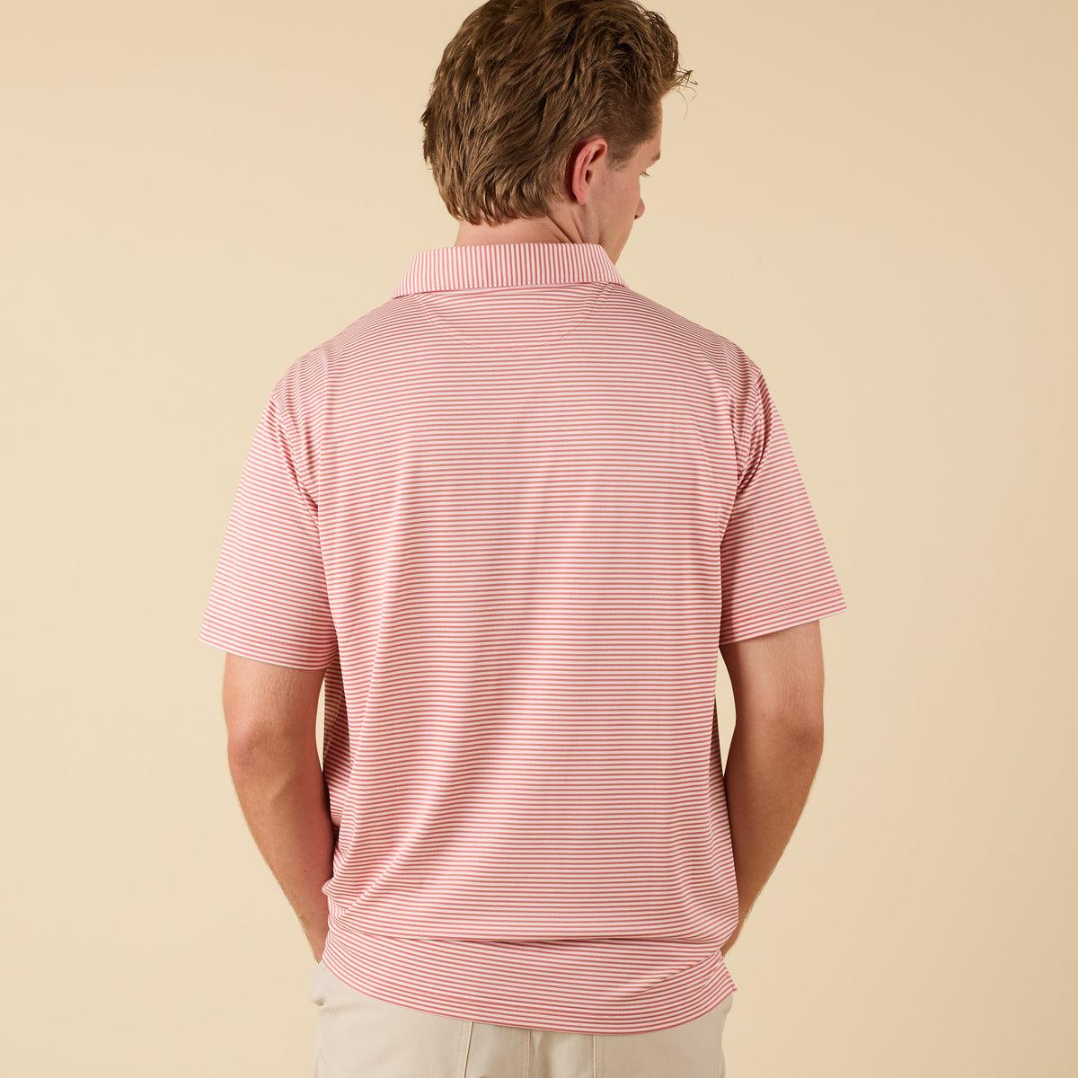 Man wearing a pink striped polo on a beige background.