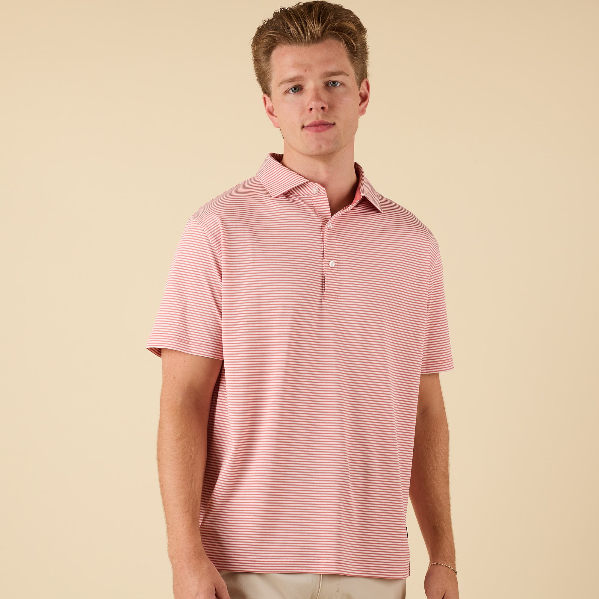 Man wearing a pink striped polo on a beige background.